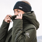 Person wearing a green coat with a brand logo, adjusting the hood against a light background